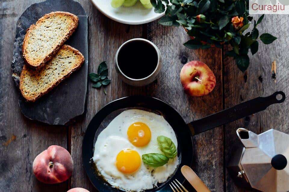 Top view of fried eggs with mint in pan near fruits and bread on wooden table