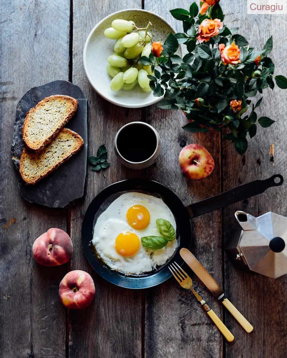 Top view of fried eggs with mint in pan near fruits and bread on wooden table