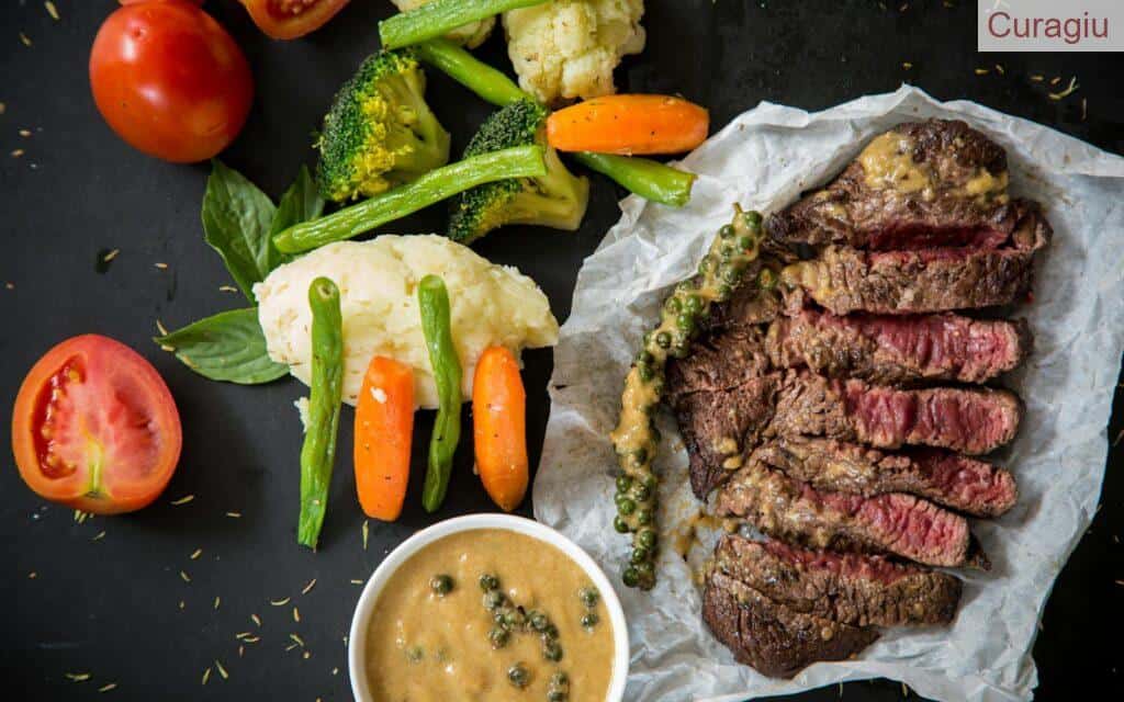 Grilled steak served with fresh vegetables and pepper sauce, presenting a colorful and appetizing meal.