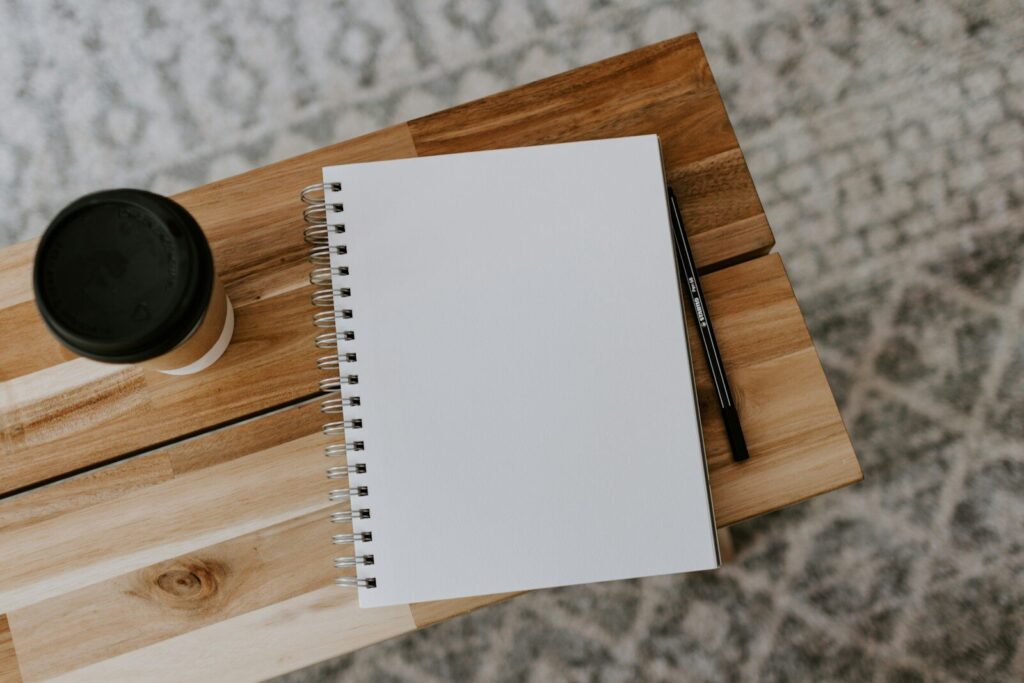 Cuaderno abierto con café junto al portátil en la mesa de redacción de Curagiu